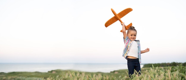 Menina ativa e saudável brinca sozinha com um avião de brinquedo em um campo de verão se lança no céu e sonha em se tornar um piloto ou aeromoça Estraga o fundo do céu infantil Banner