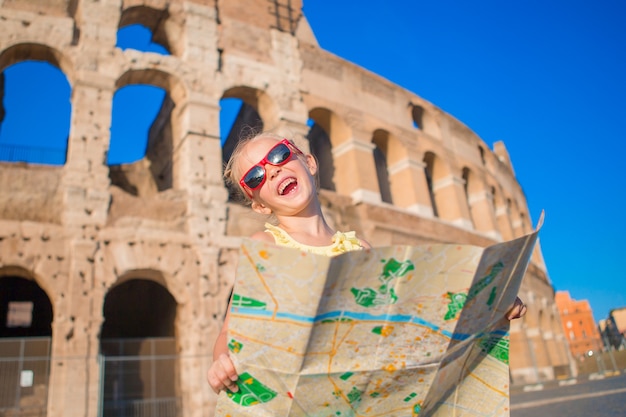 Menina ativa pequena adorável com o mapa na frente do Colosseum em Roma, Itália.