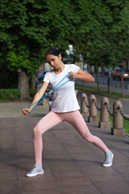 Menina atlética fazendo alongamento manual com faixa de resistência azul no parque