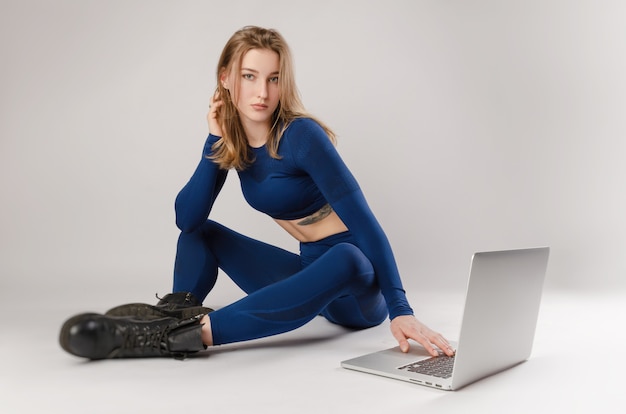 Menina atlética posando no estúdio realizando exercícios online em um laptop em um fundo branco