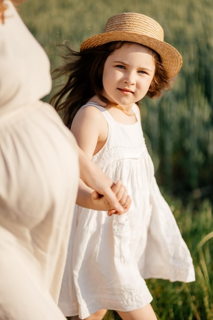 Menina atraente em um chapéu de palha está correndo em um campo de trigo com orelhas verdes