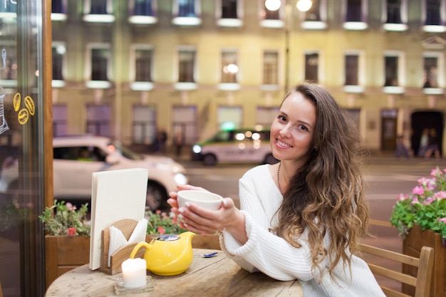 Foto menina atrativa nova que senta-se na noite em um café.