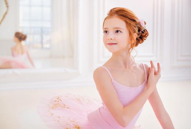 Menina bailarina em um tutu rosa e sapatilhas posando em um estúdio branco