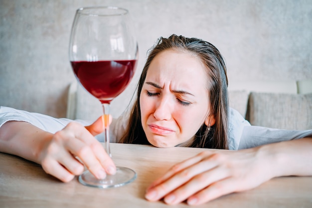 Menina bêbada bebe vinho e chora sobre a mesa.