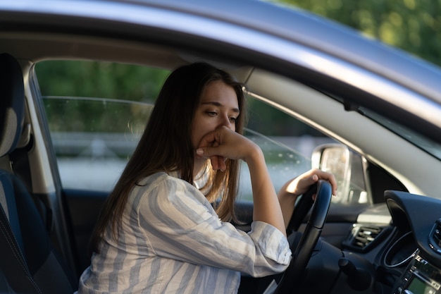 Menina bêbada dirigindo um carro, mulher jovem cansada, infeliz em um veículo, sofrendo de dor de cabeça ou transferência de mão de obra