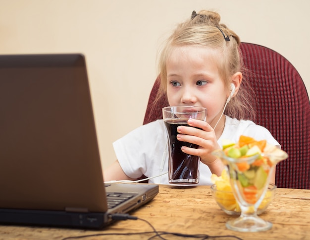 Menina bebe água com gás na frente do computador.