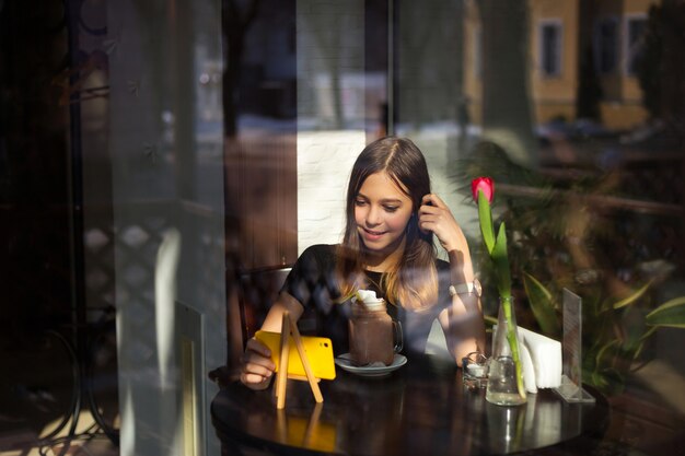 Menina bebe café e assiste vídeo no celular