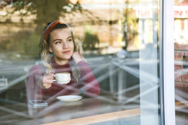 Menina bebe cappuccino em uma cafeteria, sentado em uma mesa perto da janela.