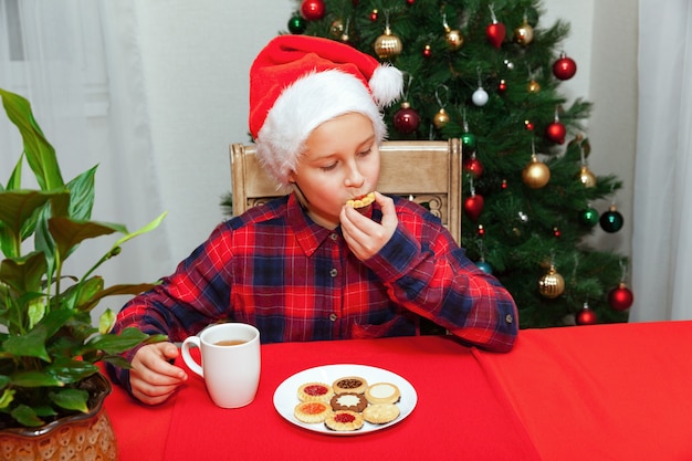 Menina bebe chá e biscoitos no fundo da árvore de Natal