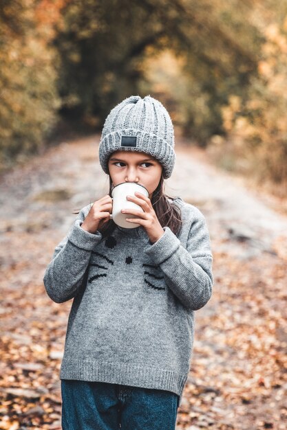 Menina bebe chá no parque de outono