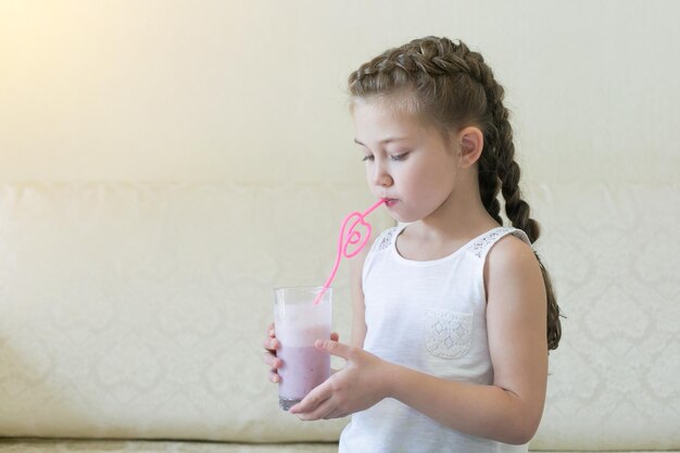 Foto menina bebendo água de um copo contra a parede