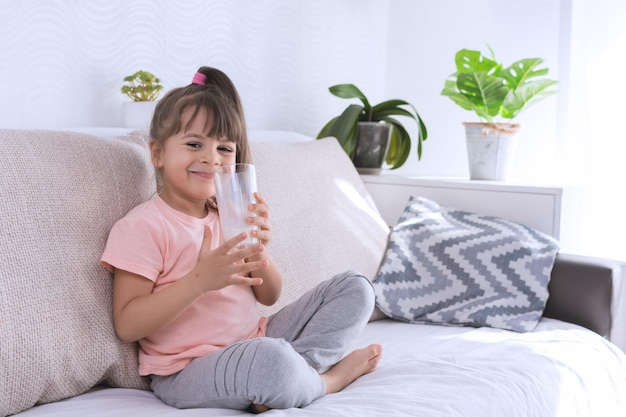 Foto menina bebendo leite saudável comendo uma criança tomando café da manhã criança conceito de sonho filha menina na cozinha bebe leite de iogurte