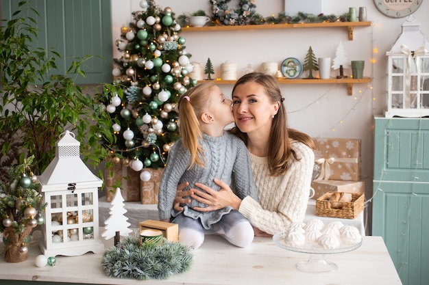 Menina beijando sua mãe enquanto está sentado na mesa da cozinha no Natal em casa.