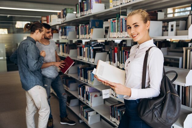 Menina bem pensativa parece estudante de pé com livro na biblioteca de uma universidade