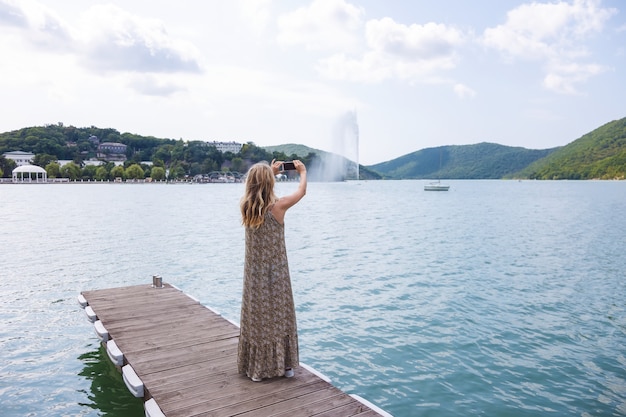 Menina blogger viajante fica no cais e tira fotos em um smartphone