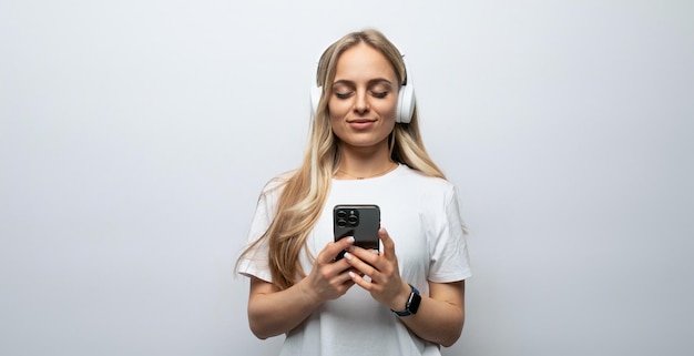 Menina blogueira com fones de ouvido na cabeça dela segurando um telefone nas mãos dela em um fundo branco