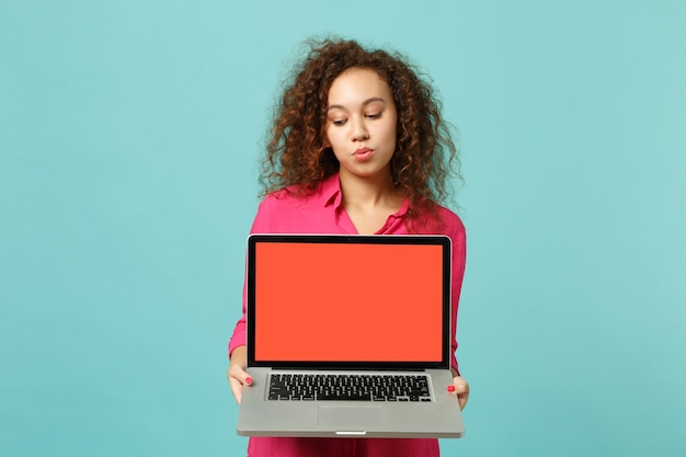 Menina bonita africana com roupas casuais segurar o computador laptop pc com tela vazia em branco isolada sobre fundo azul turquesa no estúdio. emoções sinceras de pessoas, conceito de estilo de vida. simule o espaço da cópia.