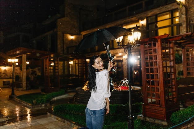 Menina bonita alegre segurando guarda-chuva enquanto passeava lá fora Ela está voltando e olhando para a câmera com verdadeiro prazer e sorriso sincero Copie o espaço no lado direito