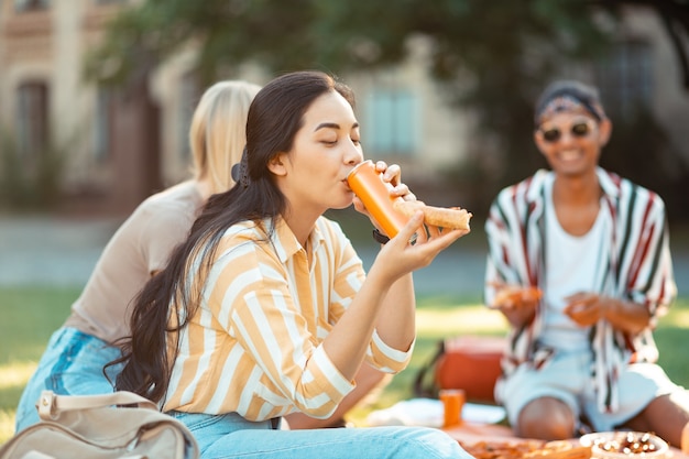 Menina bonita alegre segurando uma fatia de pizza e bebendo suco com os amigos