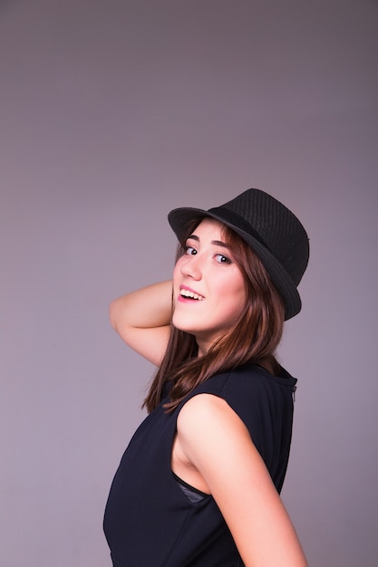 Menina bonita alegre usando vestido preto e chapéu preto clássico, sorrindo para a câmera.