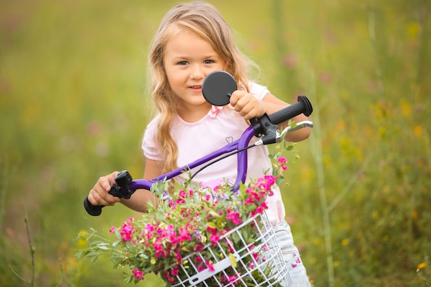 Menina bonita, andar de bicicleta com o cesto cheio de flores. Criança alegre