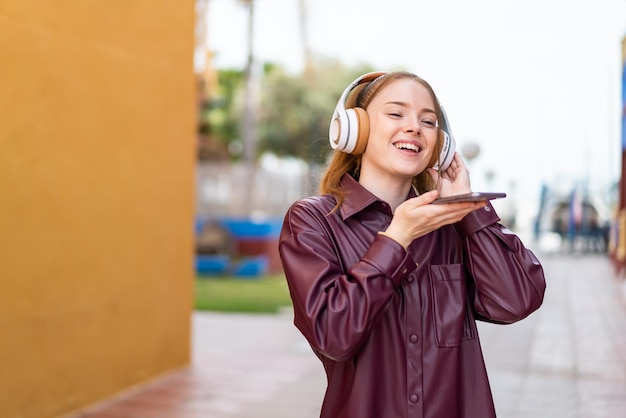 Menina bonita ao ar livre ouvindo música com um celular e cantando