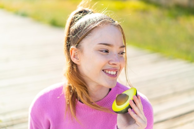 Menina bonita ao ar livre segurando um abacate com expressão feliz