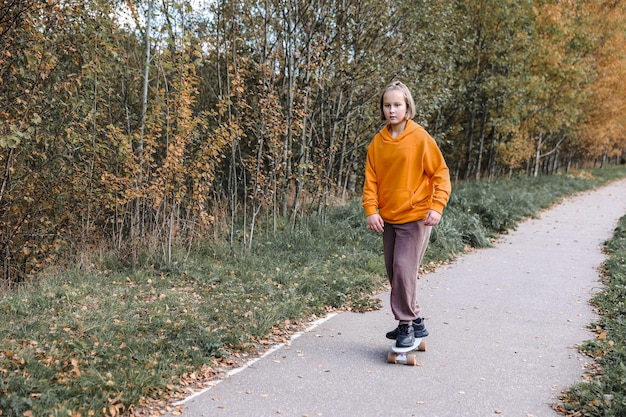 Menina bonita aprendendo a andar de skate ao ar livre em lindo dia de outono. Atividades infantis e conceito de estilo de vida ativo.