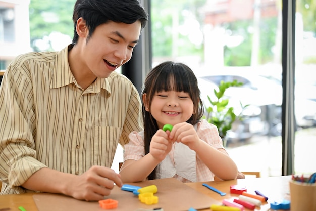 Menina bonita asiática gosta de aprender a moldar argila colorida ou jogar massa com seu professor de arte masculino