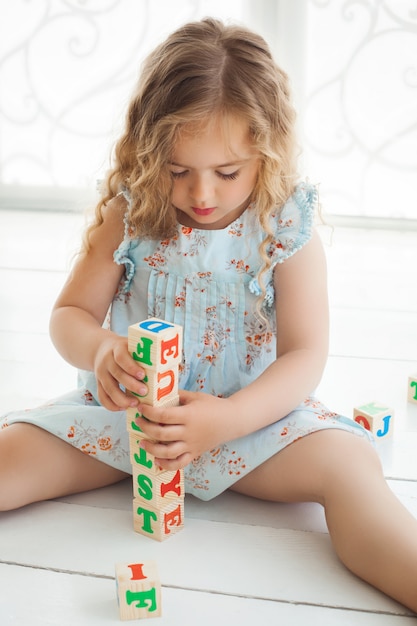 Menina bonita brincando com cubos abc e educar. Menina bonita que constrói blocos de um alfabeto. Criança brincando dentro de casa.