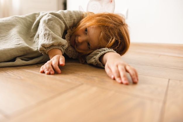 Menina bonita caucasiana com cabelo vermelho está cansada de jogar mentiras no chão dentro de casa Conceito de infância
