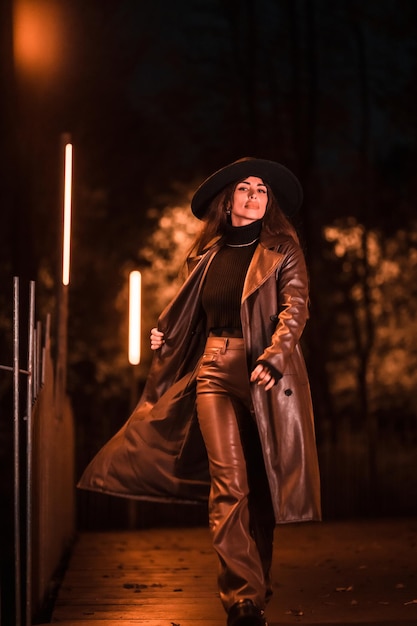 Menina bonita caucasiana com chapéu, andando à noite em um parque. Moda e estilo de vida de inverno à noite, foto vertical