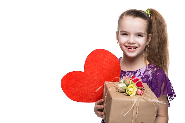 Menina bonita caucasiana em vestido de renda roxa, segurando uma caixa com um presente decorado com flores. Tiro no estúdio em fundo branco isolado