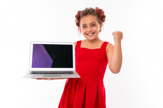 Menina bonita caucasiana no vestido vermelho mantém laptop isolado na parede branca