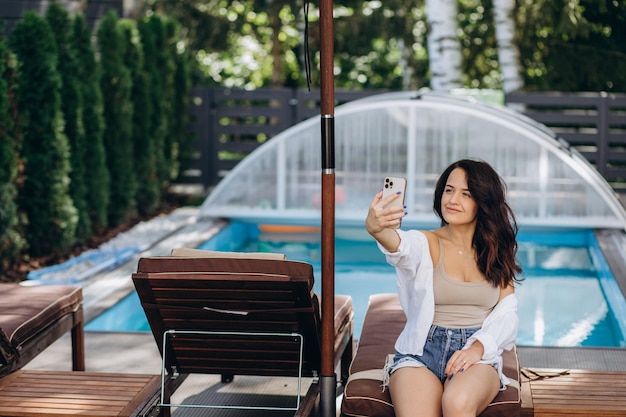 Menina bonita caucasiana tomando selfie no smartphone na piscina no resort tropical