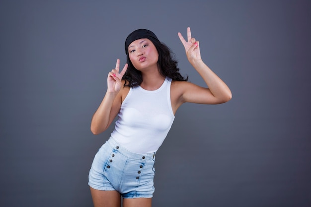 Menina bonita chinesa com bandana e shorts fazendo o símbolo da paz ou o sinal da vitória em pose engraçada