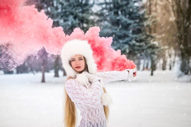 Menina bonita com bomba de fumaça de cor vermelha à disposição no dia de inverno