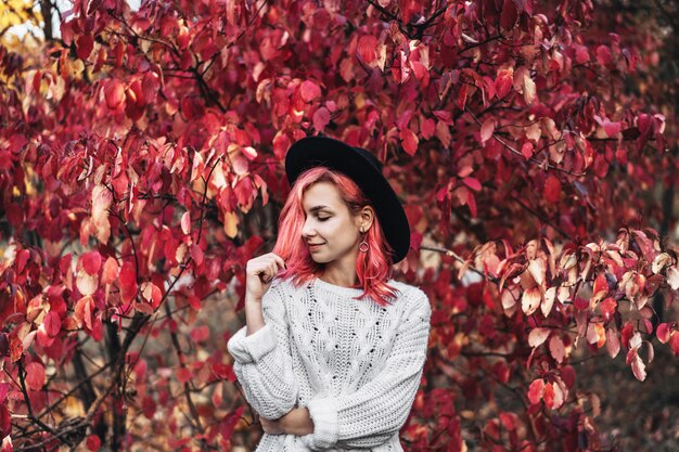 Menina bonita com cabelo vermelho e chapéu andando no parque, outono.