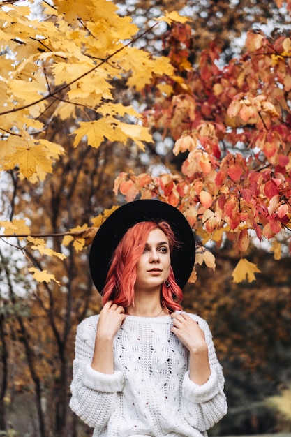 Menina bonita com cabelo vermelho e chapéu andando no parque, outono.