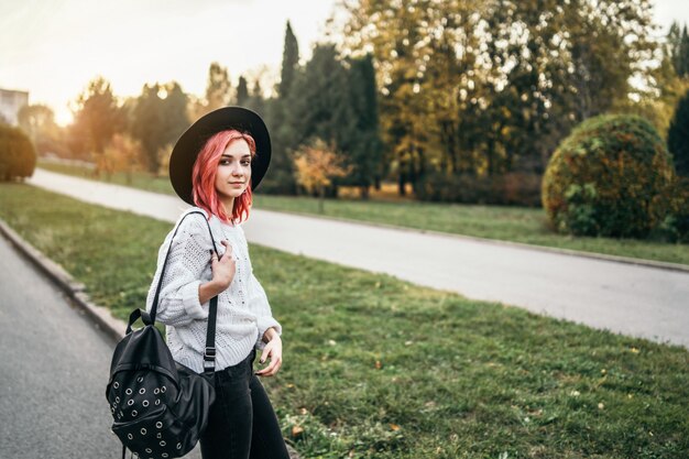 Menina bonita com cabelo vermelho e chapéu relaxante no parque, outono.