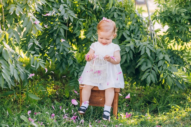 Menina bonita com cabelos loiros em um vestido branco, sentado em uma cadeira no parque ensolarado dia de verão.