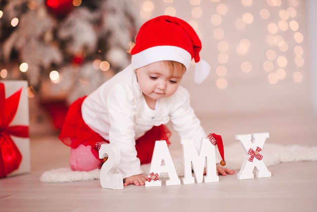 Menina bonita com chapéu de Papai Noel posando sobre fundo de Natal com letras de Natal. Concentre-se na placa de madeira.