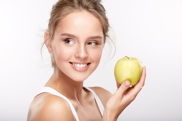 Menina bonita com dentes brancos como a neve em fundo branco studio, conceito de odontologia, sorriso perfeito, segurando a maçã e olhando para a esquerda.