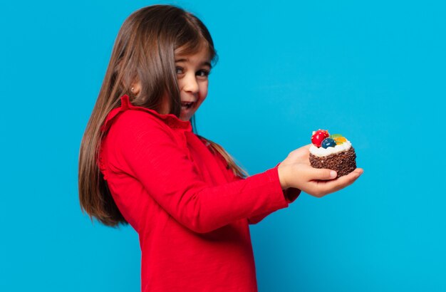 Menina bonita com expressão de surpresa e segurando um bolo de xícara