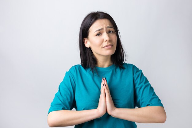 Menina bonita com expressão desamparada, pede ajuda, mantém as palmas das mãos pressionadas.