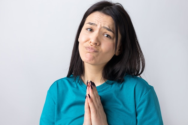 Menina bonita com expressão desamparada, pede ajuda, mantém as palmas das mãos pressionadas.