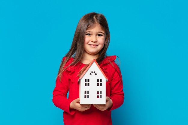 Foto menina bonita com expressão feliz e segurando um modelo de casa