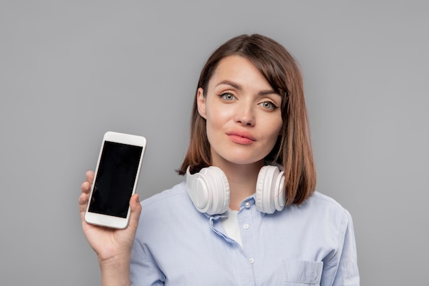 Menina bonita com fones de ouvido mostrando seu anúncio ou promoção na tela do smartphone isoladamente