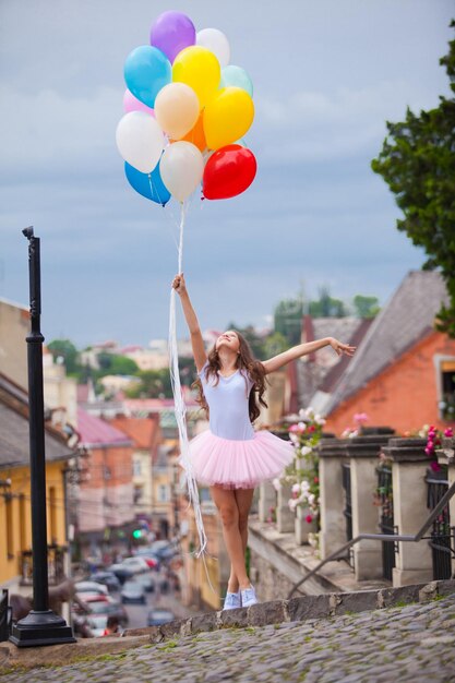 Menina bonita com grandes balões de látex coloridos posando na rua de um centro histórico