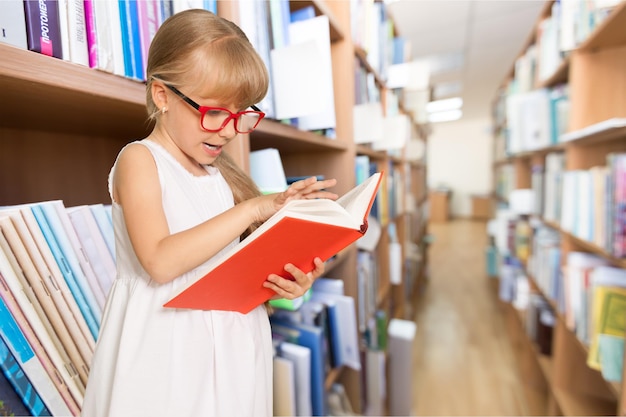 Menina bonita com livro na grande biblioteca